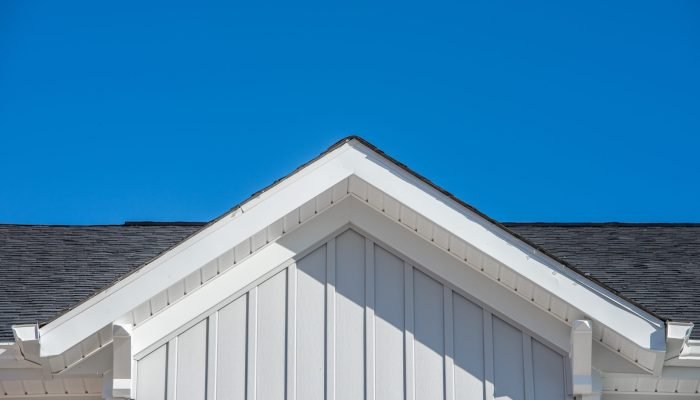 Gable roof with white fascia, gray vertical vinyl lap siding blue sky background